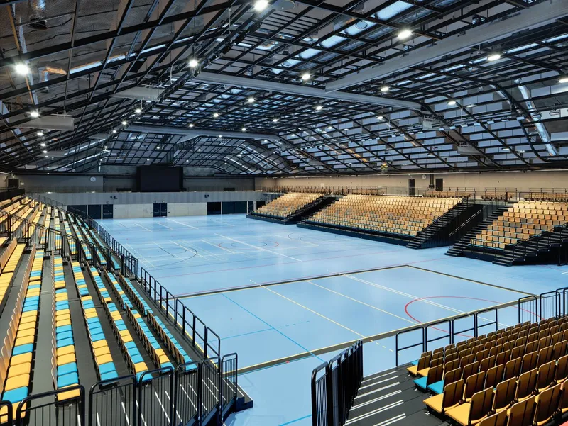 View from bleachers showing the curved steel and glass roof structure above the sports floor