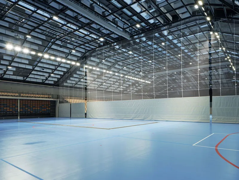 Volleyball court with retractable net divider beneath the curved glazed roof and steel trusses