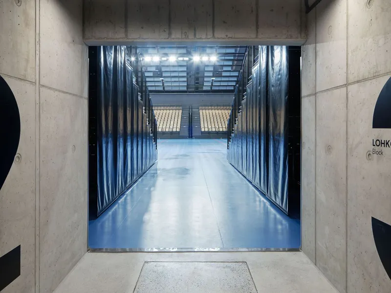 Concrete entrance threshold opening onto a polished blue resin corridor with corrugated metal walls and overhead lighting