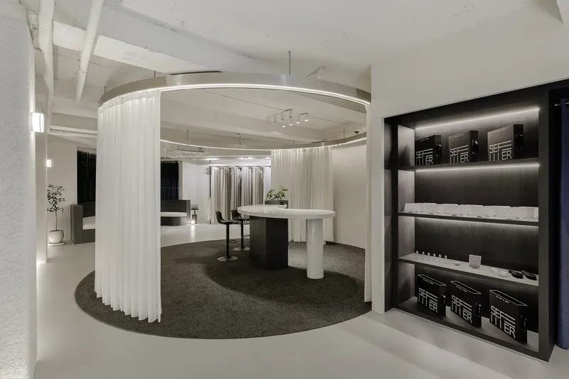Reception area with curved white curtain screen, circular table with columns, and dark product shelving