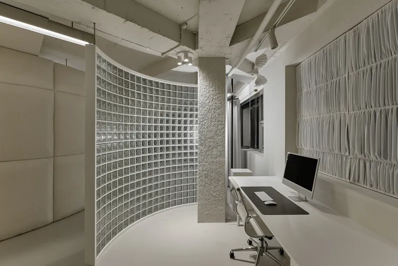 Workstation with glass block curved wall, exposed concrete ceiling beams, and white fabric panels