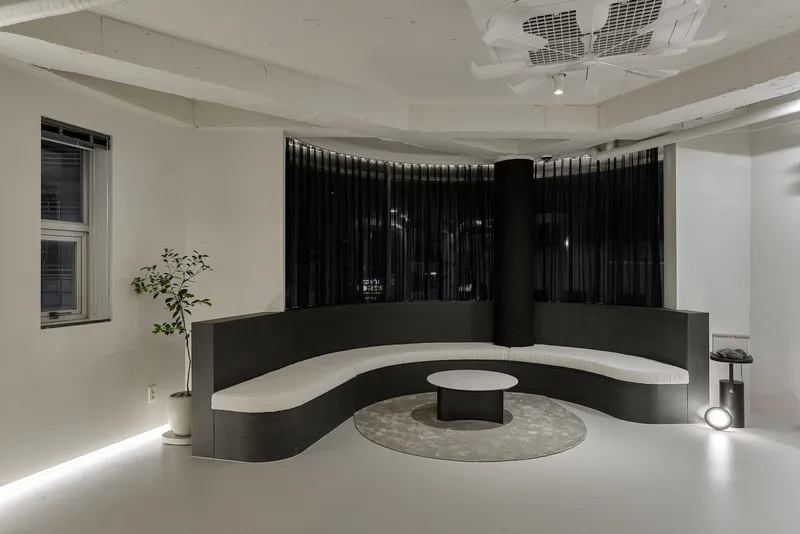 Curved black reception counter with white seating ledge and central table under exposed concrete ceiling