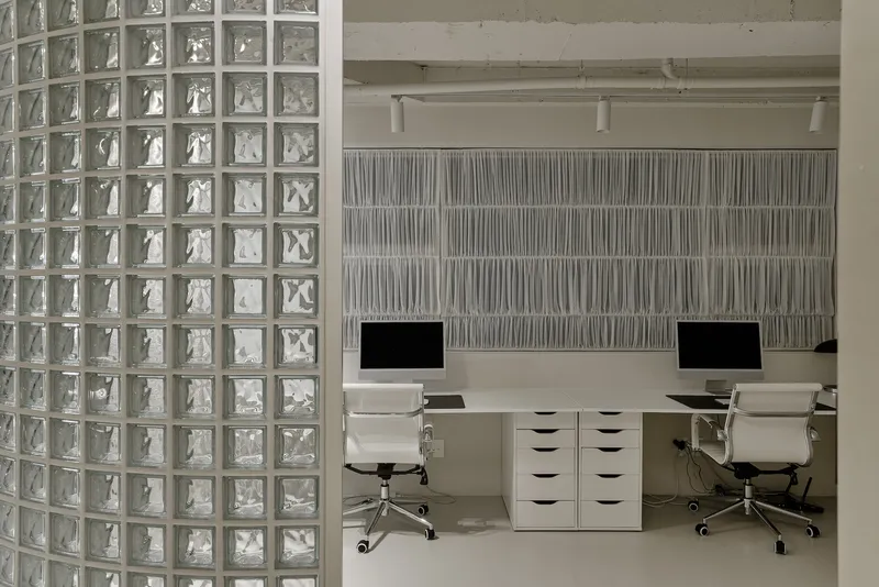 Work area with white desk units and textured wall panels behind glass block partition