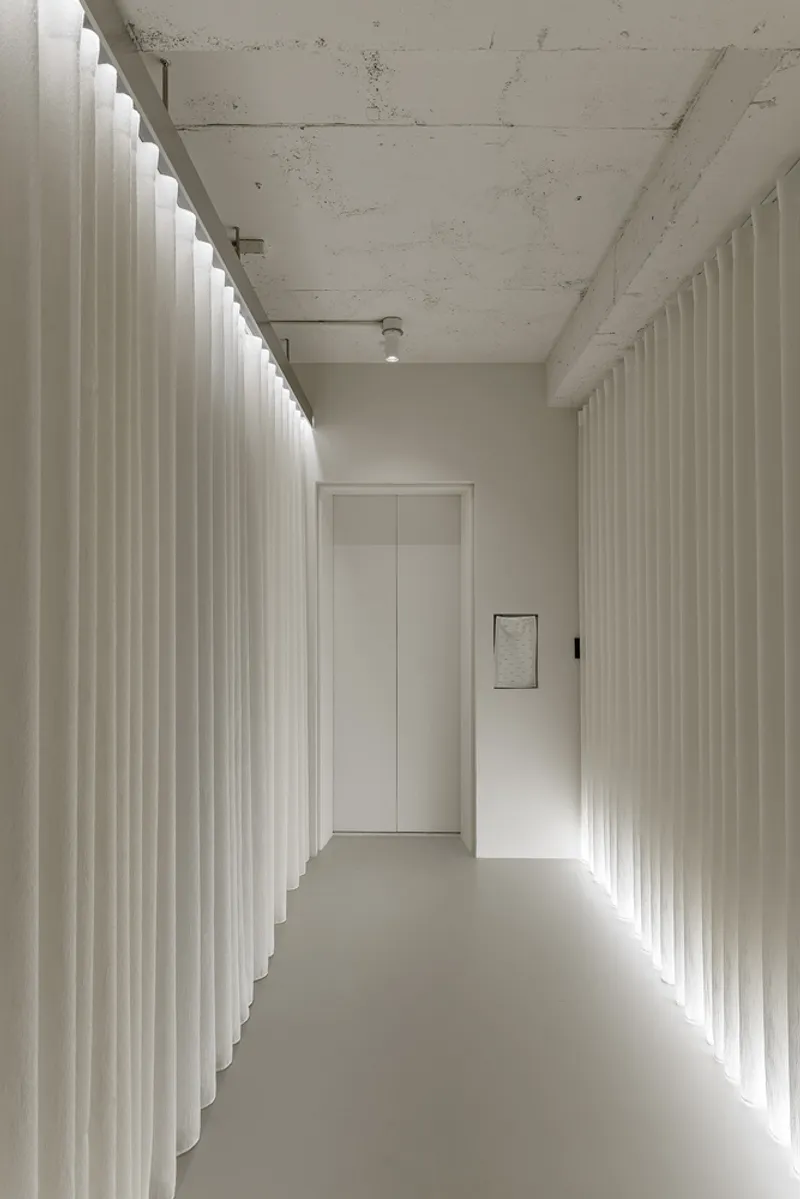 Corridor with backlit pleated curtain walls and exposed concrete ceiling beams