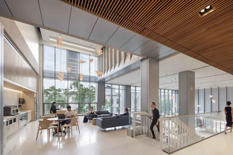 Double-height communal space with timber slat ceiling, glass railings and people gathering around tables