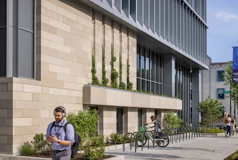 Ground-floor plaza with limestone walls, planted beds with climbing vines, and pedestrians with bicycles