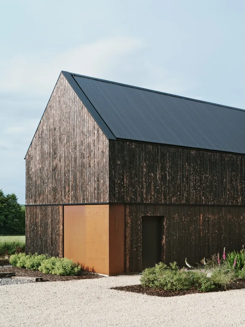 Gable volume clad in vertical charred timber with a corten steel entry panel and planted beds