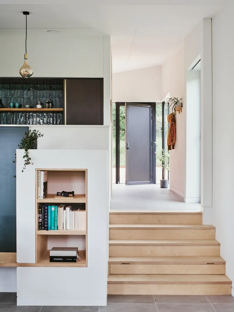 Light wood stairs descending to entry hall with built-in shelving and a coat hanging by the door