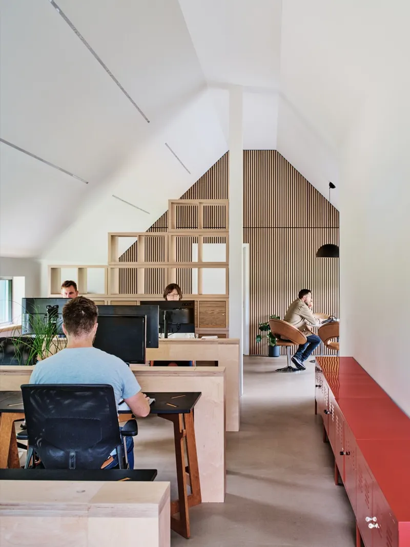 Open workspace with timber slatted partition and red storage units beneath vaulted ceiling