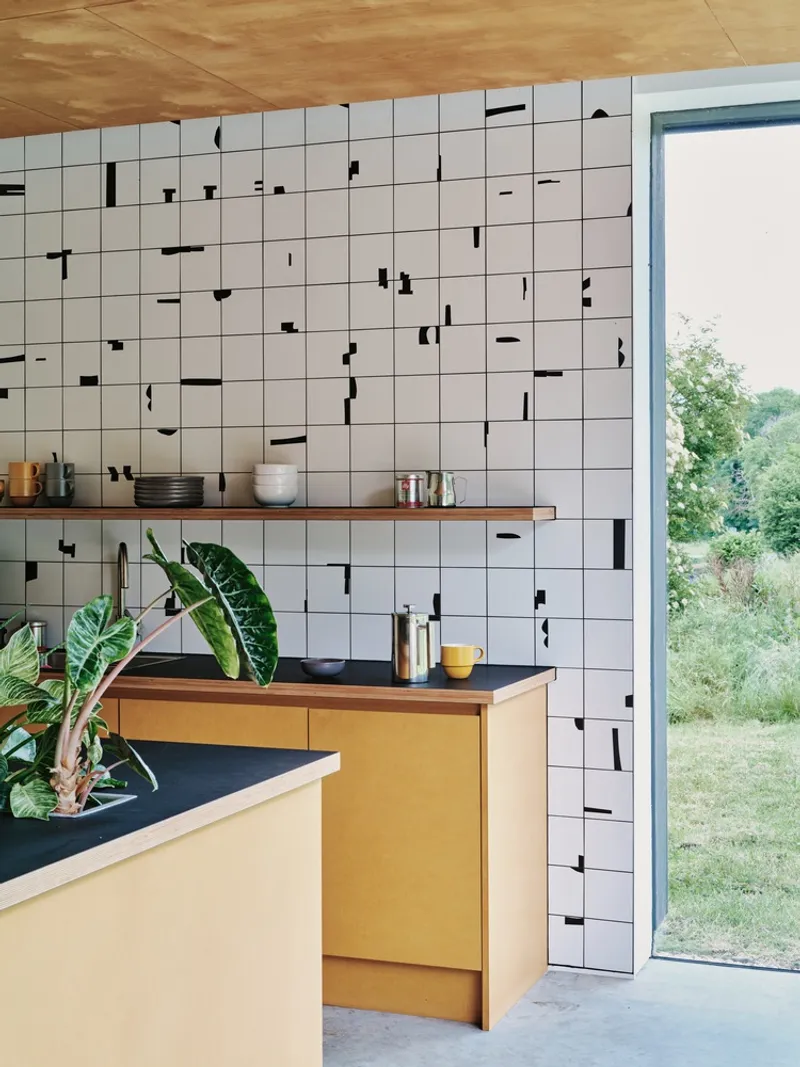 White tile wall with scattered black accent tiles behind timber shelves and garden view