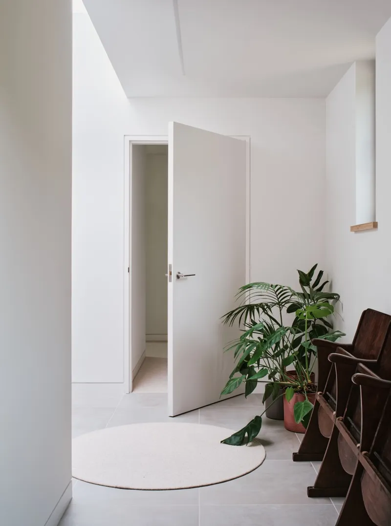 White hallway corner with open doorway and potted plants on pale floor tiles