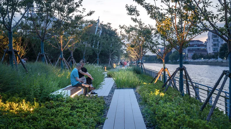 Waterside seating area with timber benches, planted grasses, and uplighting among trees at dusk
