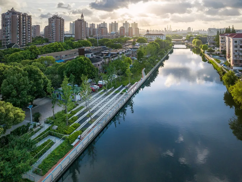 Wide canal view showing the linear park with stepped green terraces under a cloudy late afternoon sky
