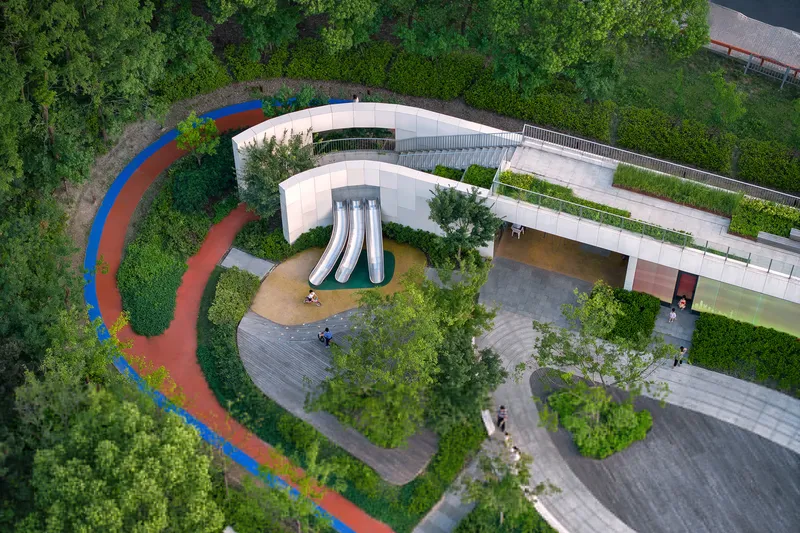 Top-down view of the playground area with three metal slides set within curved paving and planting beds