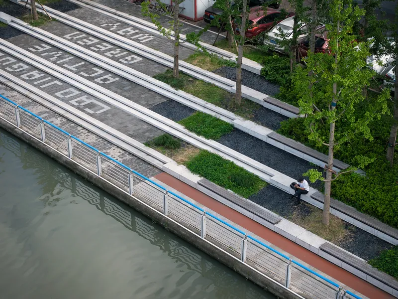 Overhead view of stepped concrete terraces with linear benches and planted strips descending toward the water's edge
