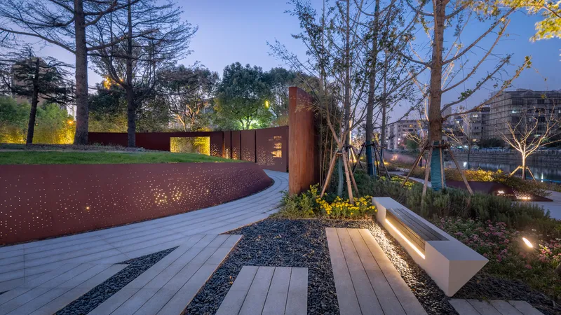 Timber boardwalk with integrated bench seating and weathering steel planters lit by ground lights at dusk