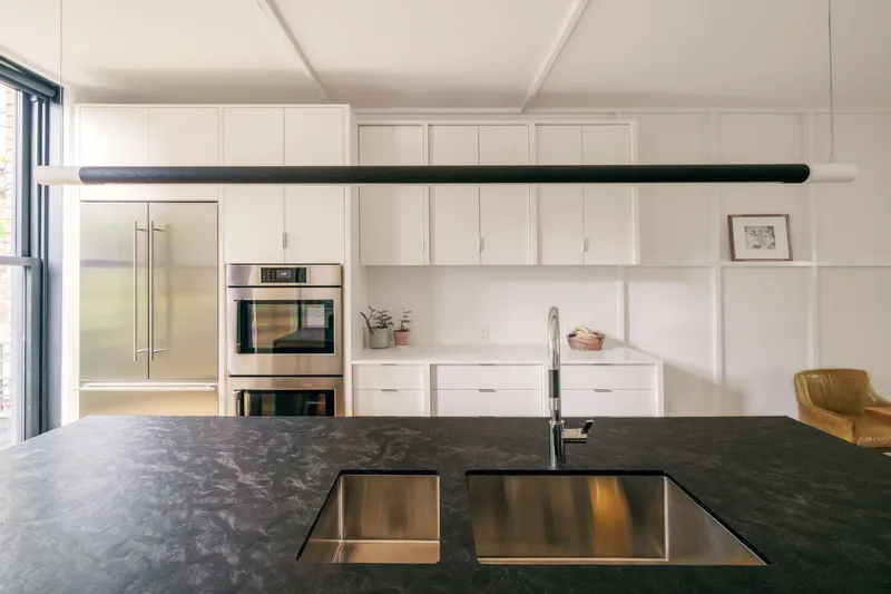 Kitchen island detail with flush stainless sinks in dark stone countertop and horizontal pendant