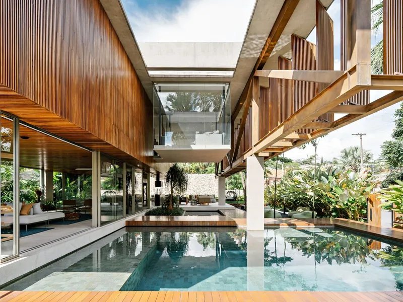 View across the pool toward the open-air concrete bridge linking timber-clad volumes under overcast sky