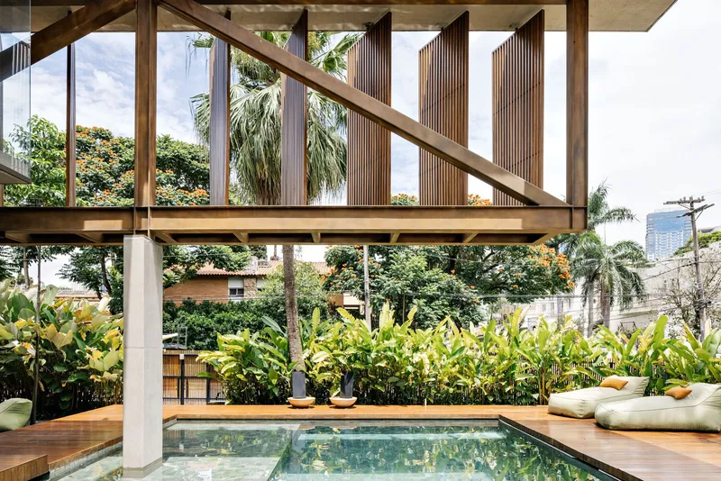 Pool terrace framed by timber columns and beams with planted beds beyond in afternoon light