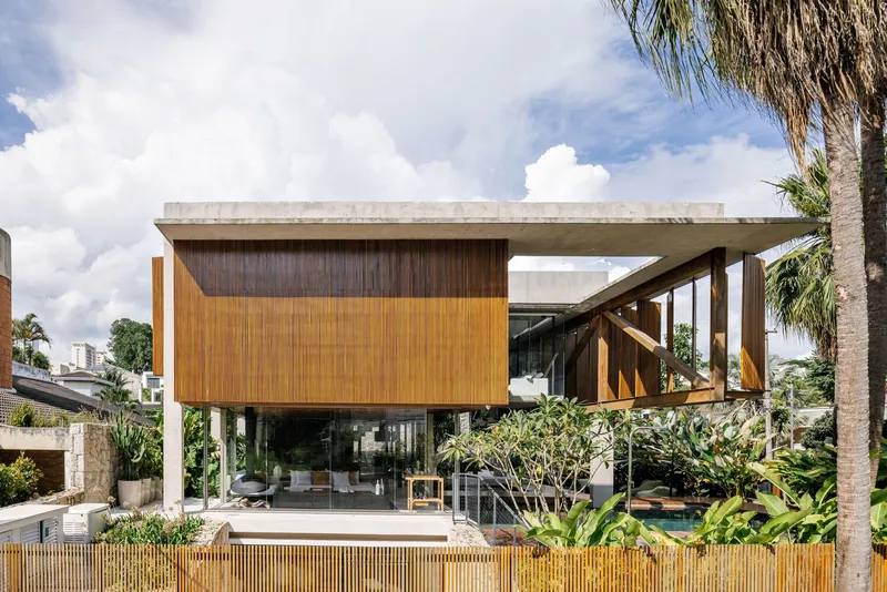 Elevated concrete and timber volumes with vertical wood cladding and a cantilevered stairway under cumulus clouds