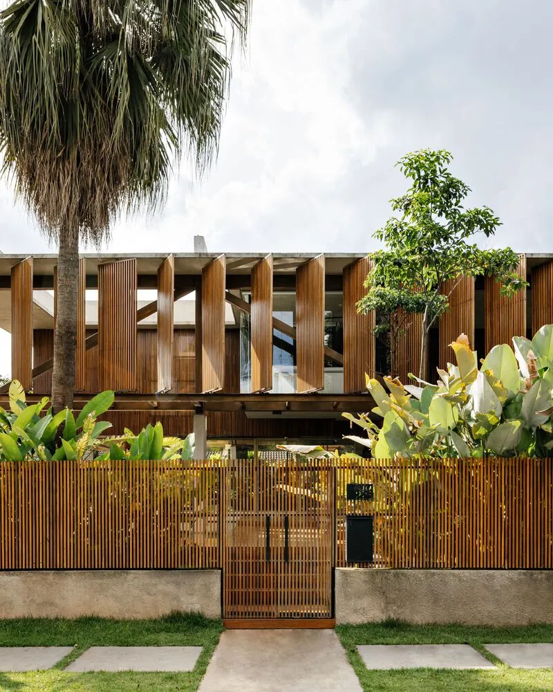 Street facade with slatted timber gate and fence framing an entry path flanked by palm trees