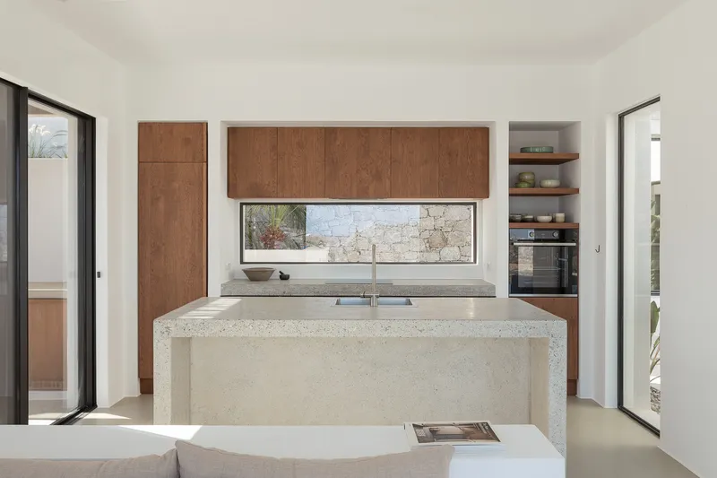 Kitchen with terrazzo island, timber cabinetry and horizontal window overlooking the stone courtyard wall