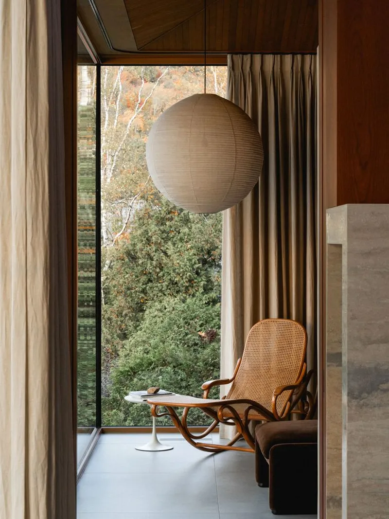 Reading nook with bentwood rocking chair positioned beside floor-to-ceiling window overlooking autumn garden