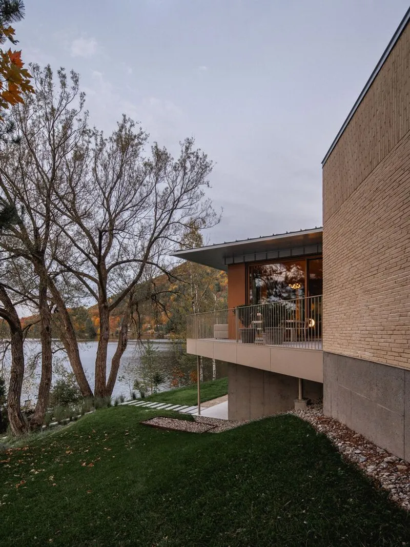 Cantilevered balcony with metal railing overlooking a lake framed by bare autumn trees