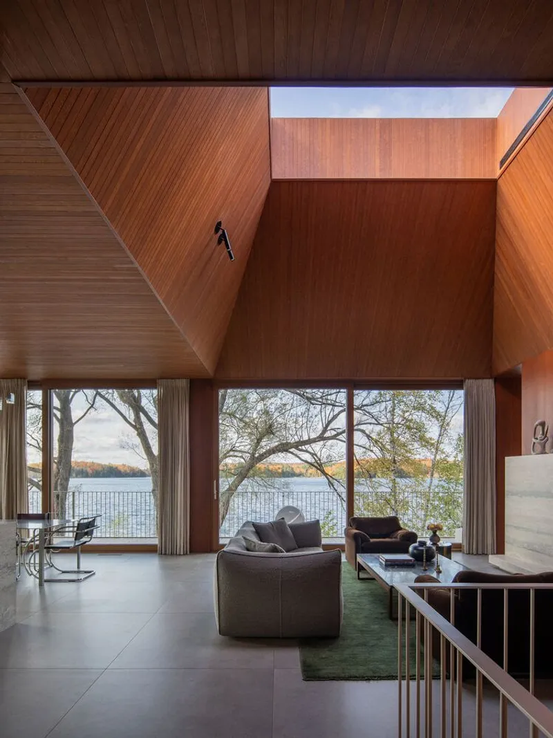 Double-height living room with angled timber ceiling and floor-to-ceiling windows facing the lake
