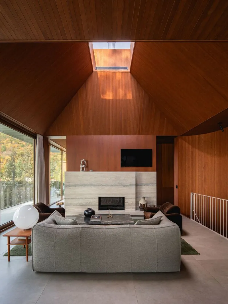 Double-height living room with wood-clad ceiling, skylight, board-formed concrete fireplace and railing to lower level