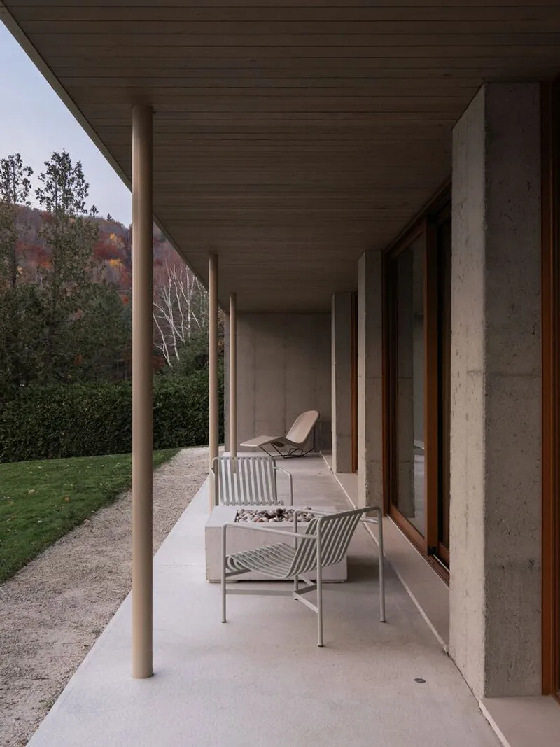 Covered terrace with slender white columns and concrete ceiling overlooking hillside vegetation in autumn