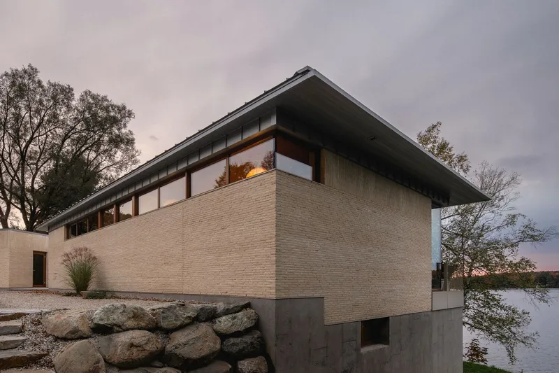 Corner view of the brick and concrete facade with clerestory windows at dusk beside the lake