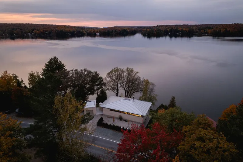 Aerial view of the low-slung roof nestled among fall foliage along the lakeshore at sunset