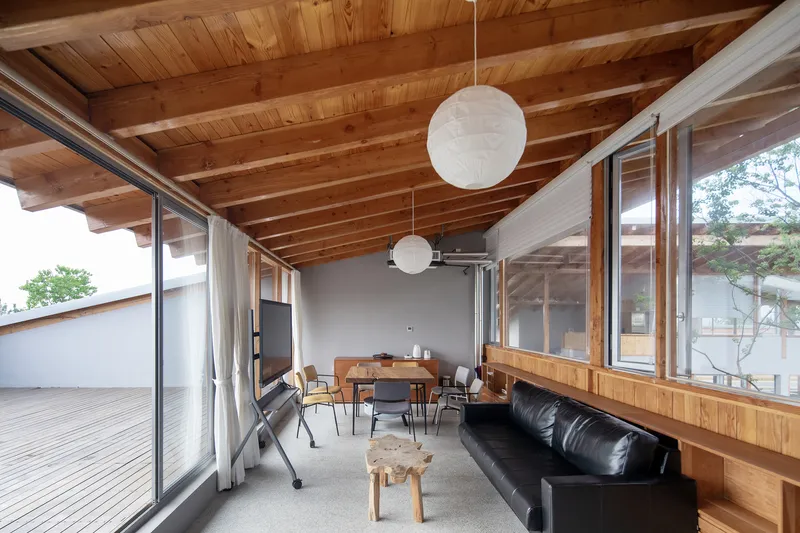 Interior living space with exposed timber ceiling beams, spherical pendant lights and glazed walls opening to a courtyard