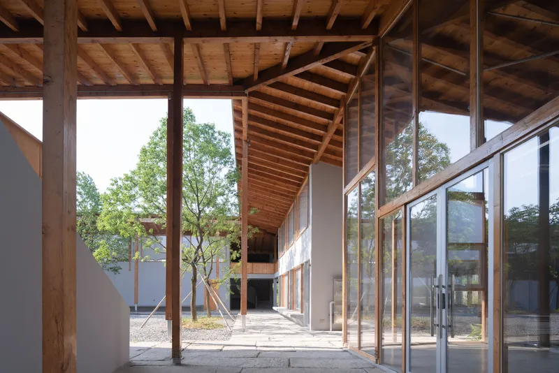 Covered walkway with timber post and beam structure framing views of a planted courtyard with young trees