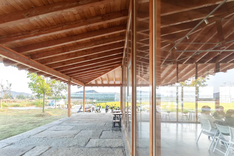 Covered exterior terrace with exposed timber rafters and floor-to-ceiling glazing overlooking a lawn