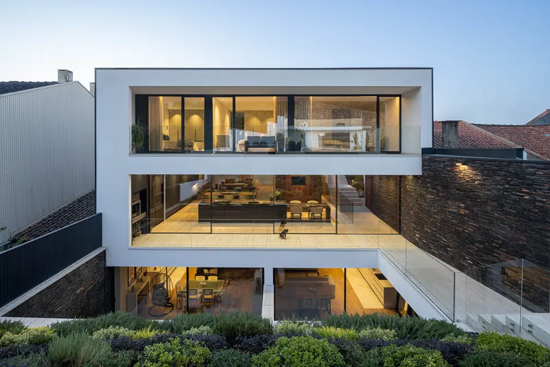 Rear elevation showing three stacked glazed volumes with illuminated interiors at dusk