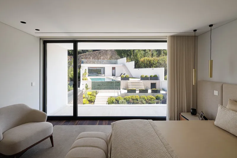 Bedroom with full-height glazed doors opening to a terraced garden with pool and planted beds