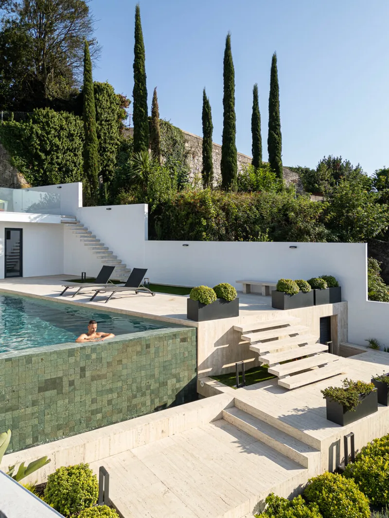 Terraced pool with green mosaic tile surround and stone steps leading down through planted beds