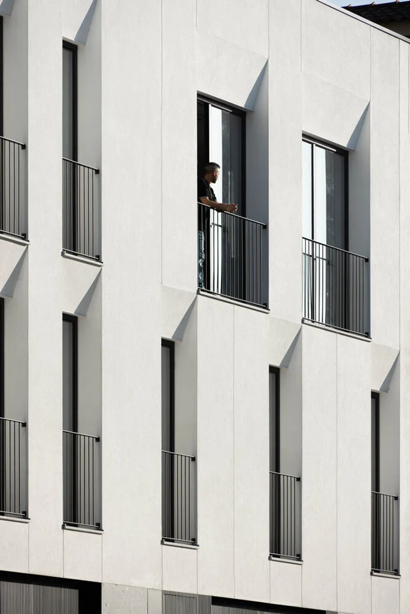 White panel facade with recessed balcony openings and a person standing in the doorway