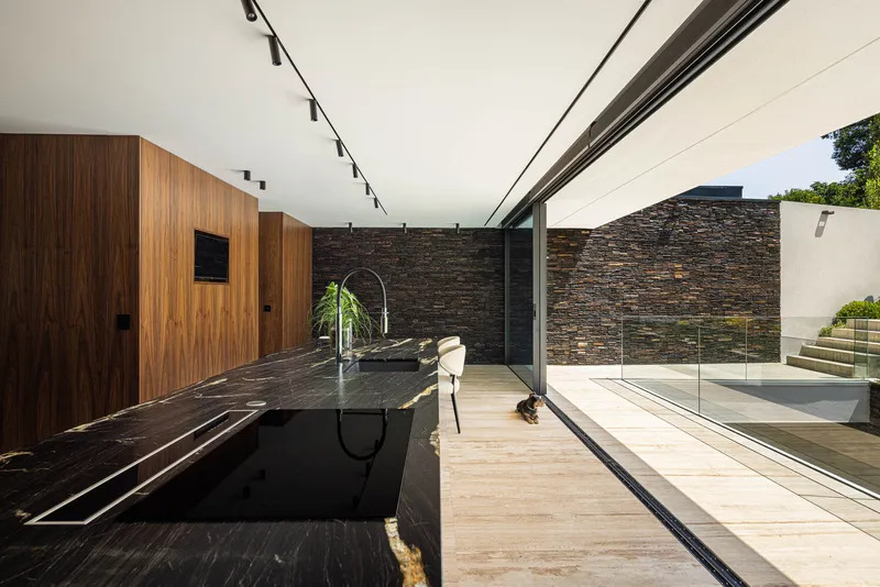 Kitchen counter with dark stone surface opening to a terrace through a sliding glass wall