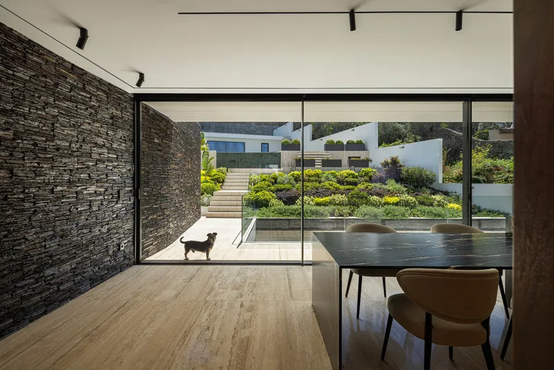 Glazed dining room opening to terraced garden with dog on the stone patio in summer