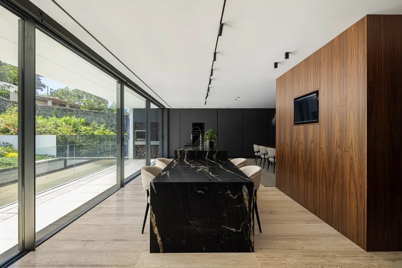 Dining space with black marble waterfall edge table and floor-to-ceiling sliding glass doors to garden