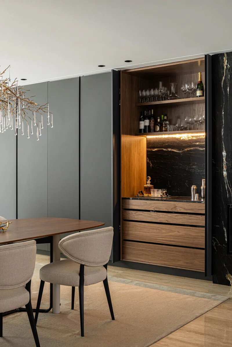 Bar niche with illuminated shelving and black marble backsplash set within grey paneled storage wall