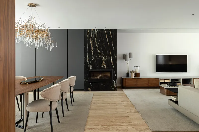 Open-plan living space with black marble fireplace surround and walnut dining table under a branched chandelier