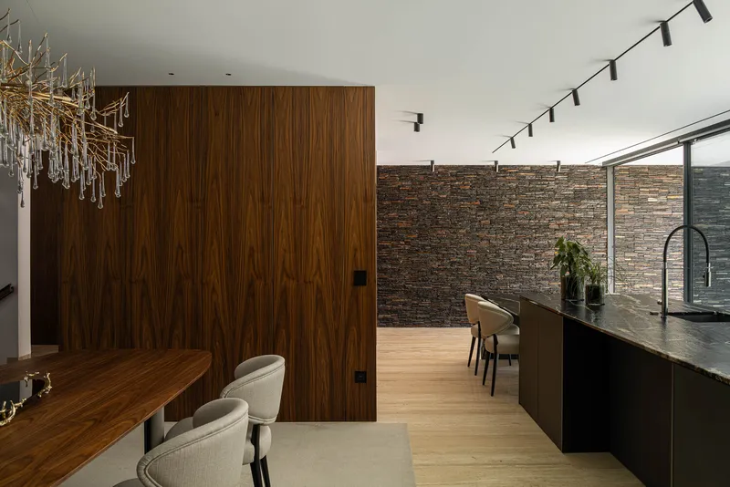Open plan dining area with walnut veneer partition wall and track lighting above black kitchen island