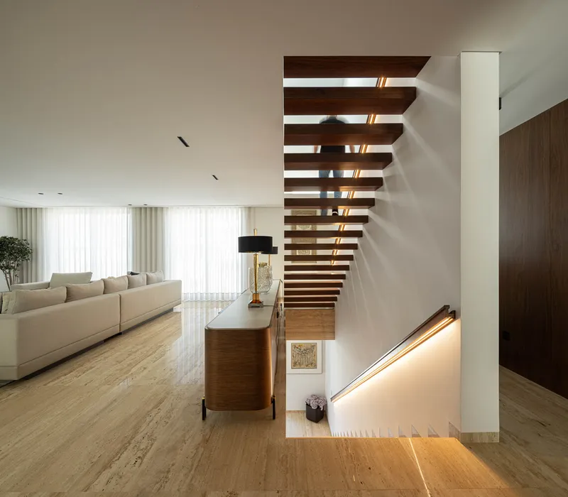 Open tread timber staircase rising between two levels with indirect lighting below the handrail