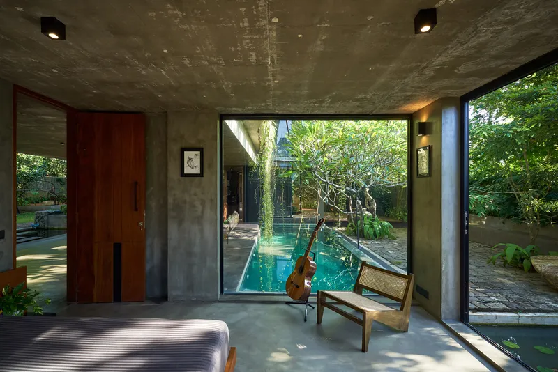 Bedroom interior looking through glazed walls toward the central courtyard pool and vine-covered tree at midday