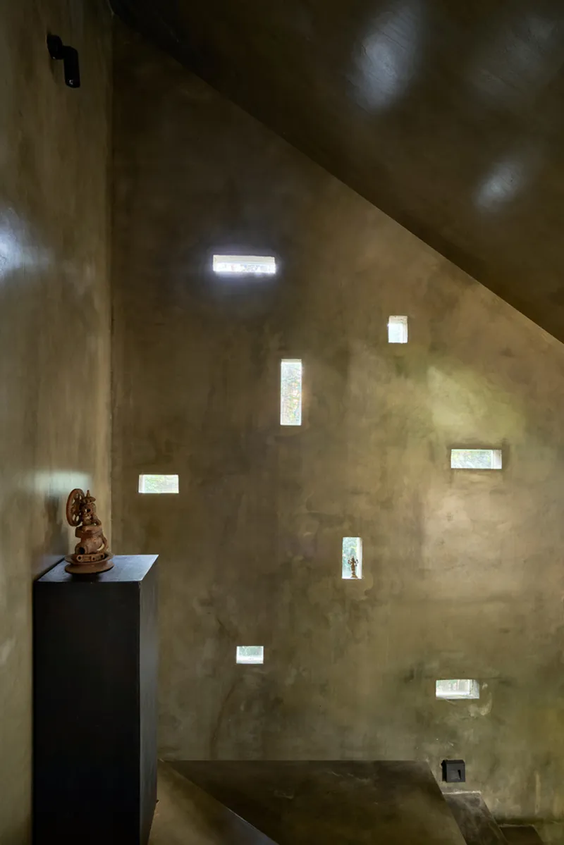 Interior corner wall with scattered rectangular apertures framing light and a sculpture on black pedestal