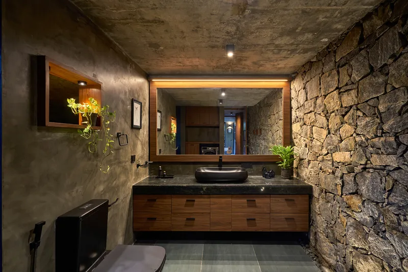 Bathroom vanity with timber cabinetry, black basin, and rustic stone accent wall under concrete ceiling